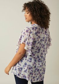 Blumenbluse aus leichtem, transparenter Stoff in Weiß mit lila und blauen Blumen, kurzen Rüschensäumen und einer lockeren Passform.