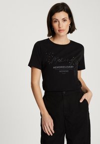 Czarna bawełniana koszulka z nadrukiem sloganu "Tworzymy Wspomnienia Każdy Weekend" z złotymi akcentami i krótkimi rękawami. Połączona z czarnymi spodniami.