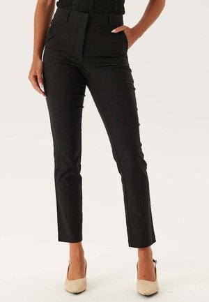 Pantaloni neri su misura con vestibilità slim, vita alta, chiusura con zip e passanti per cintura; abbinati a tacchi color beige per un look raffinato.