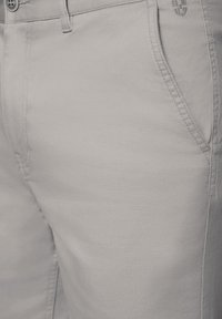 Jasnoszare bawełniane spodnie z teksturowanym wykończeniem, z kieszeniami z przodu, zapięciem na guzik i subtelnymi detalami przeszycia.