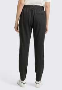 Grijze gestreepte broek met een elastische tailleband en een achterzak, met een taps toelopend ontwerp en een gladde textuur. Gecombineerd met witte sneakers.