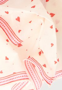 Ροζ ύφασμα με μικρά κόκκινα μοτίβα καρδιάς και κόκκινες ριγωτές άκρες, χαλαρά διπλωμένο που δείχνει την υφή και τις λεπτομέρειες του σχεδίου.