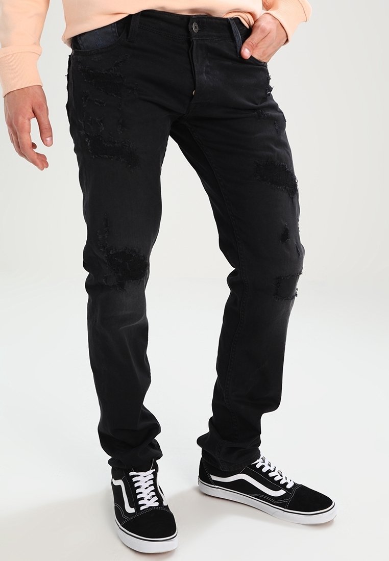 Sorte denimjeans med slidte pletter, slank pasform, fem-lomme design og kontrasterende syninger. Båret med sorte og hvide sneakers.