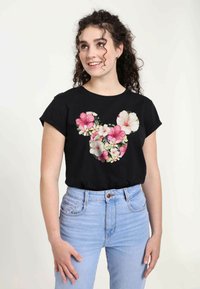 Sort t-shirt med et blomsterdesign i pink og hvid, formet som et Mickey Mouse-hoved. Kortærmet og afslappet fit, parret med lyseblå jeans.
