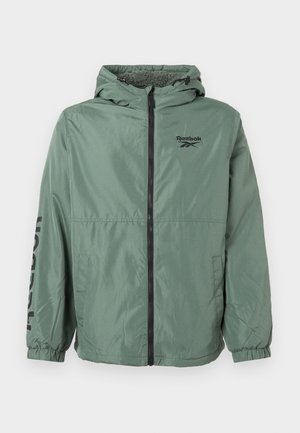 Jaqueta leve verde com capuz, apresentando um zíper preto e um grande logo da Reebok na manga. Punhos elásticos e dois bolsos laterais.