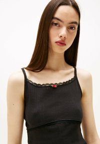 Top de tirantes negro con detalles de encaje y una pequeña rosa roja en el escote; el textil presenta un sutil patrón de rayas.