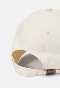 Cream cotton baseball cap with stitched accents, curved brim, and adjustable strap featuring a metal clasp on the back.