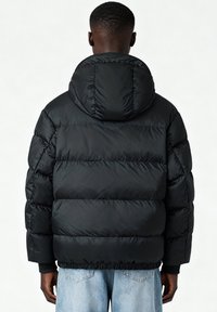 Veste matelassée noire avec capuche, présentant une texture matelassée, des poignets élastiques et un ourlet resserré. Vue de dos.