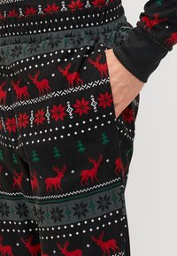 Black pants featuring a festive pattern of red reindeer, green trees, and white snowflakes. Textured fabric with an elastic waistband.
