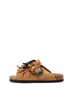 Sandalo a ciabatta in camoscio color nocciola con grande fibbia, frange e perline rotonde colorate sulla parte superiore e suola piatta nera.
