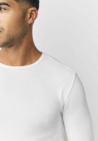 White long-sleeve ribbed shirt with a round neckline. Slim fit, smooth texture, and clean design without additional patterns or details.