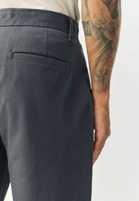 Mørkeblå bukser lavet af et glat, let stof. Har en flad baglomme, slim fit og diskrete sømdetaljer.