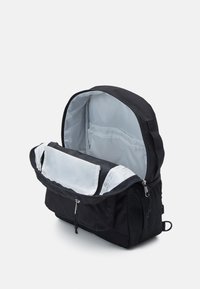 Sac à dos noir avec un sommet arrondi, doté d'un grand compartiment principal zippé et d'un intérieur gris clair. Comprend des poches latérales en maille et une poche zippée à l'avant.