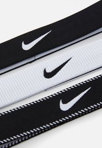 Tri elastične gumice za kosu: dvije crne s bijelim Nike logom, jedna bijela rebrasta gumica s crnim logom. Ravni dizajn, glatka tekstura.