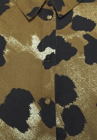 Braune und schwarze Button-Down-Hemd mit strukturiertem Stoff und gepunktetem Druck sowie schwarzen Knöpfen entlang der Vorderseite.