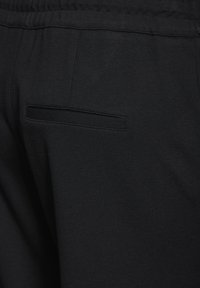 Svarta träningsbyxor med en slät yta, utrustade med ett elastiskt midjeband och en diskret bakficka med en sydd klaff.