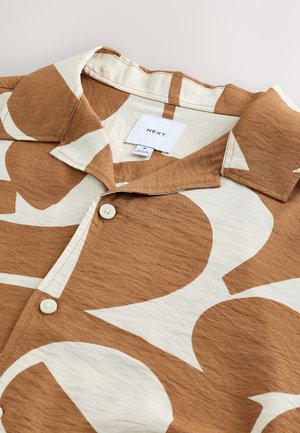 Camicia a maniche corte marrone con grandi motivi astratti bianchi. Presenta un colletto e bottoni bianchi, realizzata in tessuto strutturato. Etichetta del marchio visibile.