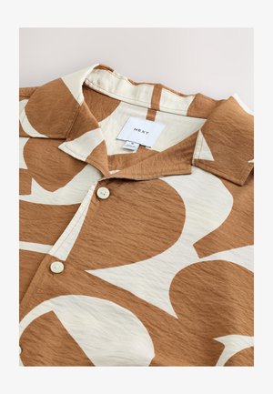 Camicia a maniche corte marrone con grandi motivi astratti bianchi. Presenta un colletto e bottoni bianchi, realizzata in tessuto strutturato. Etichetta del marchio visibile.
