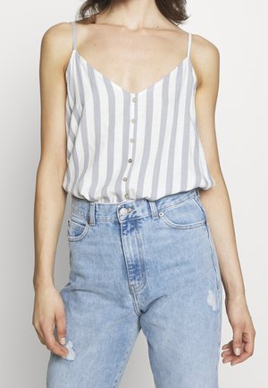 Femme portant un chemisier sans manches rayé verticalement, boutonné, rentré dans un jean déchiré bleu clair taille haute.