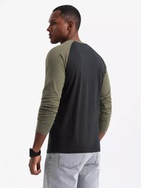 Schwarzes und olivgrünes Langarmhemd mit Raglan-Design. Verfügt über eine glatte Textur und kontrastierende Ärmel, kombiniert mit hellen Jeans.