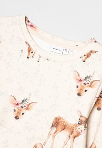 Helebeež pikkade varrukatega särk, millel on lilleline hirveprint. Pehme puuvillane materjal, ümar kaelus ja mittestruktureeritud lõige.