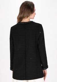 Jachetă texturată neagră cu mâneci lungi, având un guler rotund și broderii subtile. Are o croială dreaptă și detalii desfăcute la manșete.