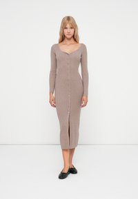 Μακριά, ριμπ πλεκτή φόρμα σε ανοιχτό καφέ χρώμα με V λαιμόκοψη, μακριά μανίκια, κουμπιά μπροστά και σχισμή στο κ άτω μέρος. Φοριέται με μαύρες μπαλαρίνες.