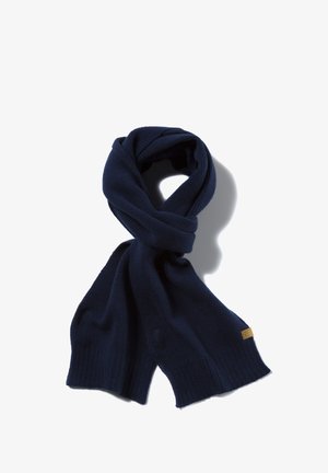 Navy blue knit scarf made of soft yarn, featuring ribbed ends and a small branded label, gently twisted in a loose loop.