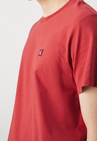 Rød bomulds-T-shirt med rund hals, korte ærmer og et lille broderet logo på venstre bryst. Glat tekstur og afslappet pasform.