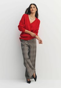 Red knit sweater with a deep V-neck and ribbed cuffs, paired with gray plaid wide-leg trousers and black pointed-toe heels.