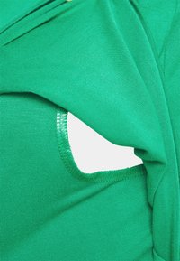 Tecido verde com um recorte redondo. Textura suave com um leve brilho, bordas acabadas e um design ajustado.