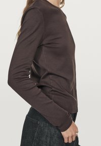 Brun langærmet skjorte lavet af blødt stof, med rund halsudskæring og en tætsiddende pasform. Sammen med mørk denim, der fremhæver en slank silhuet.