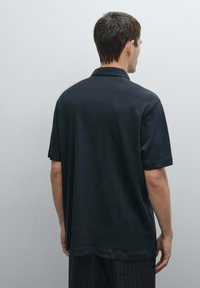 Svart polo shirt med avslappnad passform, korta ärmar och klassisk krage. Slät textur, inga synliga mönster eller logotyper.