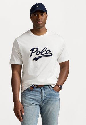 White cotton t-shirt with navy "Polo Ralph Lauren" logo. Paired with light blue denim jeans and a navy cap. Accented with a brown belt.