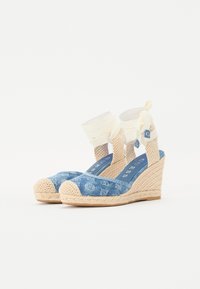 Denim kilestyvler med vævet jute-sål, lukket tå og ankelstropper i cremefarvet stof. Blå logo-mønster på overdelen.