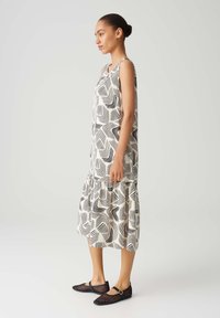 Sleeveless dress with a black and white wavy line pattern, gathered hem, and a relaxed fit. Paired with black perforated flat shoes.