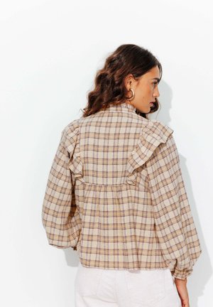 Blouse à carreaux en tissu beige avec des lignes violettes et bleues. Présente des détails froncés le long des épaules et des manches bouffantes.