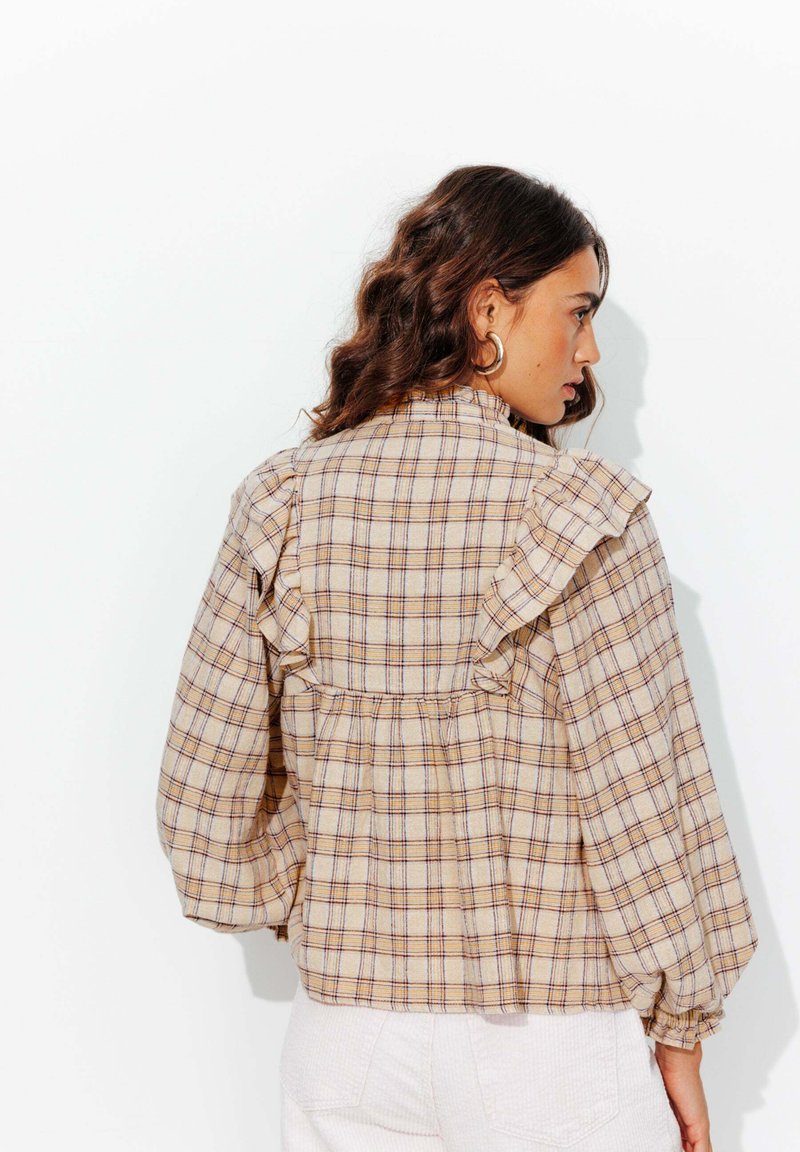 Blouse à carreaux en tissu beige avec des lignes violettes et bleues. Présente des détails froncés le long des épaules et des manches bouffantes.