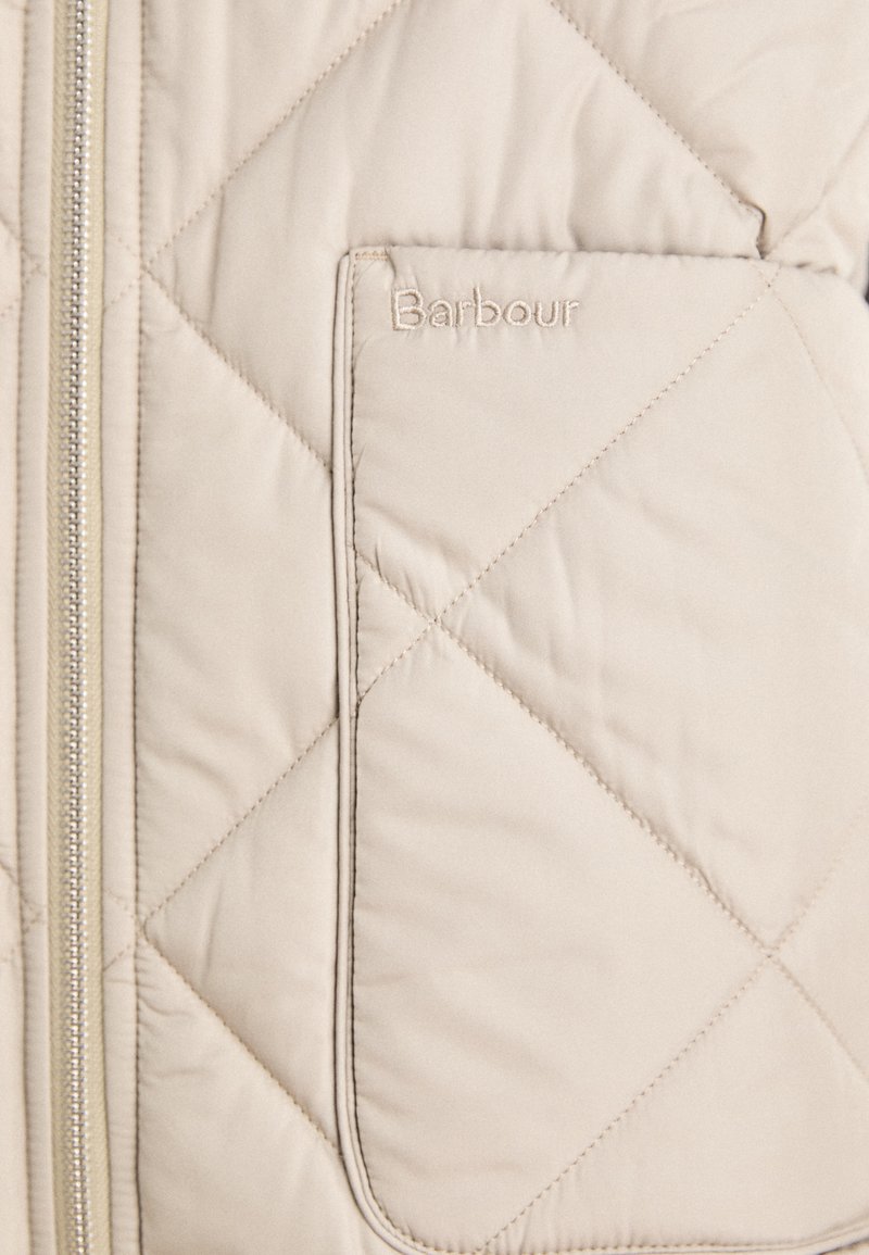 Beige gesteppte Pufferjacke mit einem Reißverschluss, ausgestattet mit einer Brusttasche und geprägtem Logo auf der Tasche. Weicher Stoff.