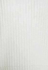Gros plan sur un tissu tricoté blanc avec une texture côtelée, montrant des motifs de points verticaux et horizontaux.