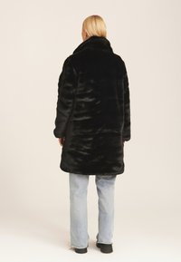 Black faux fur coat with a high collar, featuring long sleeves and a relaxed fit. Worn with light blue straight-leg jeans.