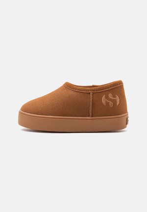 Καφέ παπούτσι slip-on από μαλακό σουέντ υλικό, με χοντρή καουτσούκ σόλα και ραμμένο λογότυπο στο πλάι, εμφανιζόμενο σε απλό φωτεινό φόντο.