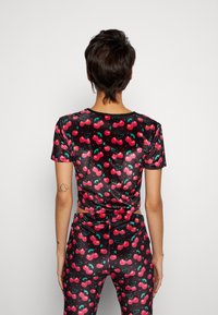Top cropped de veludo preto e calças combinando com um padrão de cerejas, apresentando folhas verdes e corações vermelhos para um design divertido.