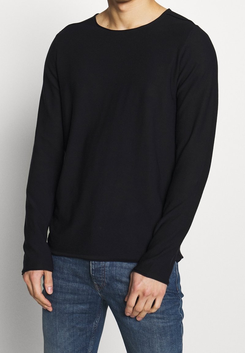 Svart långärmad skjorta av mjukt, elastiskt tyg, med rundad halsringning och lätta sidslitsar i fållen för ökad rörelsefrihet.