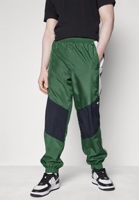 Gröna och marinblå träningsbyxor med elastisk midja, smala muddar och kontrasterande paneler; har Nike-logga på sidan.