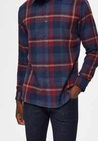 Flanellskjorta med ett blått och vinrött rutor, med knäppning fram och långa ärmar, tillverkad av mjukt texturerat material.