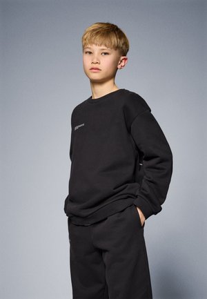 Black sweatshirt with a round neck and loose fit, featuring a white text detail on the front. Paired with matching black pants.