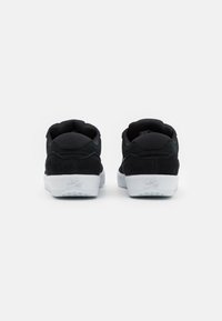Black suede sneakers with white rubber soles feature a padded collar and heel, showcasing a minimalist design with logo accents.