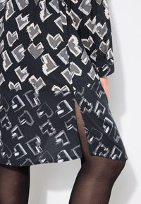 Abito nero con un motivo di forme astratte in grigio e bianco, con uno spacco laterale e maniche lunghe. Texture del tessuto morbida.