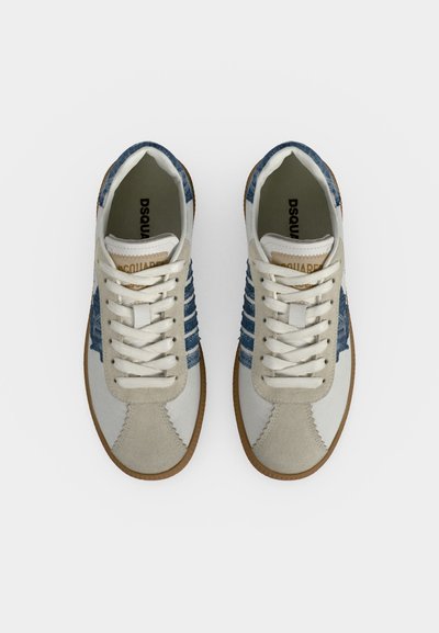 Paire de sneakers blanches et bleues à lacets avec détails en daim beige et semelles en gomme vues de dessus sur fond blanc.